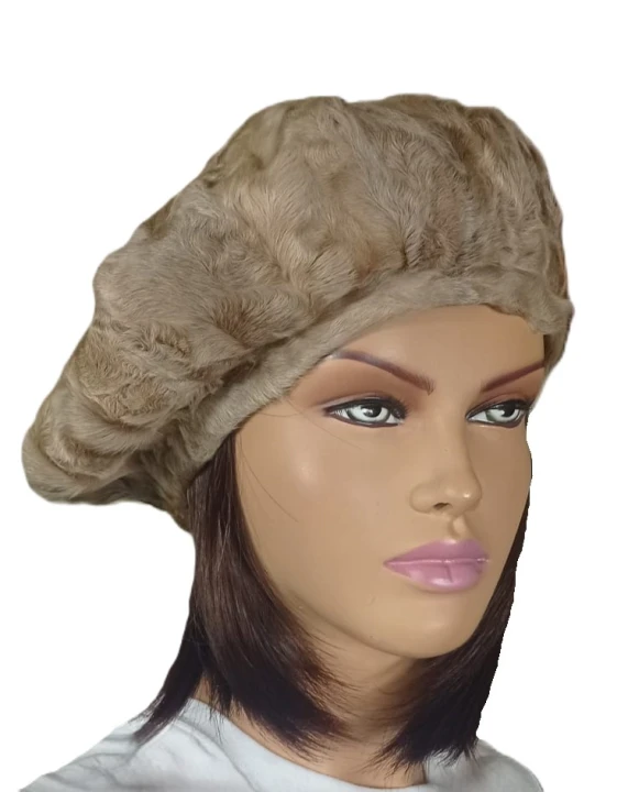 Luksusowy damski beret z naturalnego futra karakułów w beżowym odcieniu, eksponowany na pluszowej poduszce w ekskluzywnym butiku kuśnierskim, na tle wiszących futer.